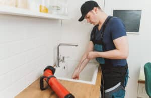 clogged_kitchen_drain_cleaning Professional drain cleaning technician clearing a stubborn clog from a residential kitchen sink using an electric drain auger.