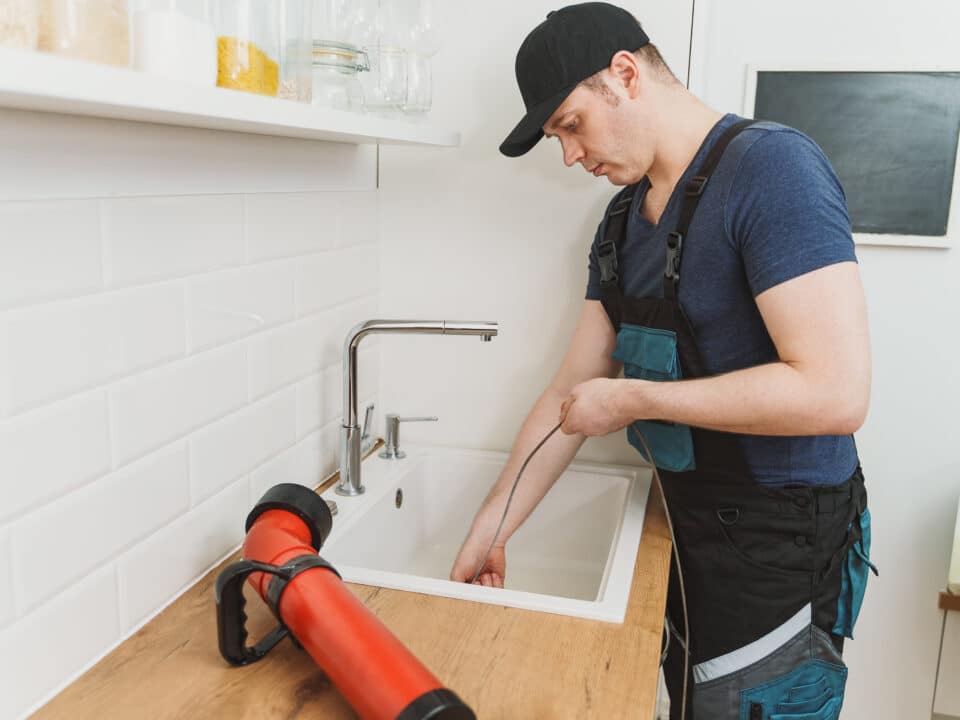 Professional drain cleaning technician clearing a stubborn clog from a residential kitchen sink using an electric drain auger.